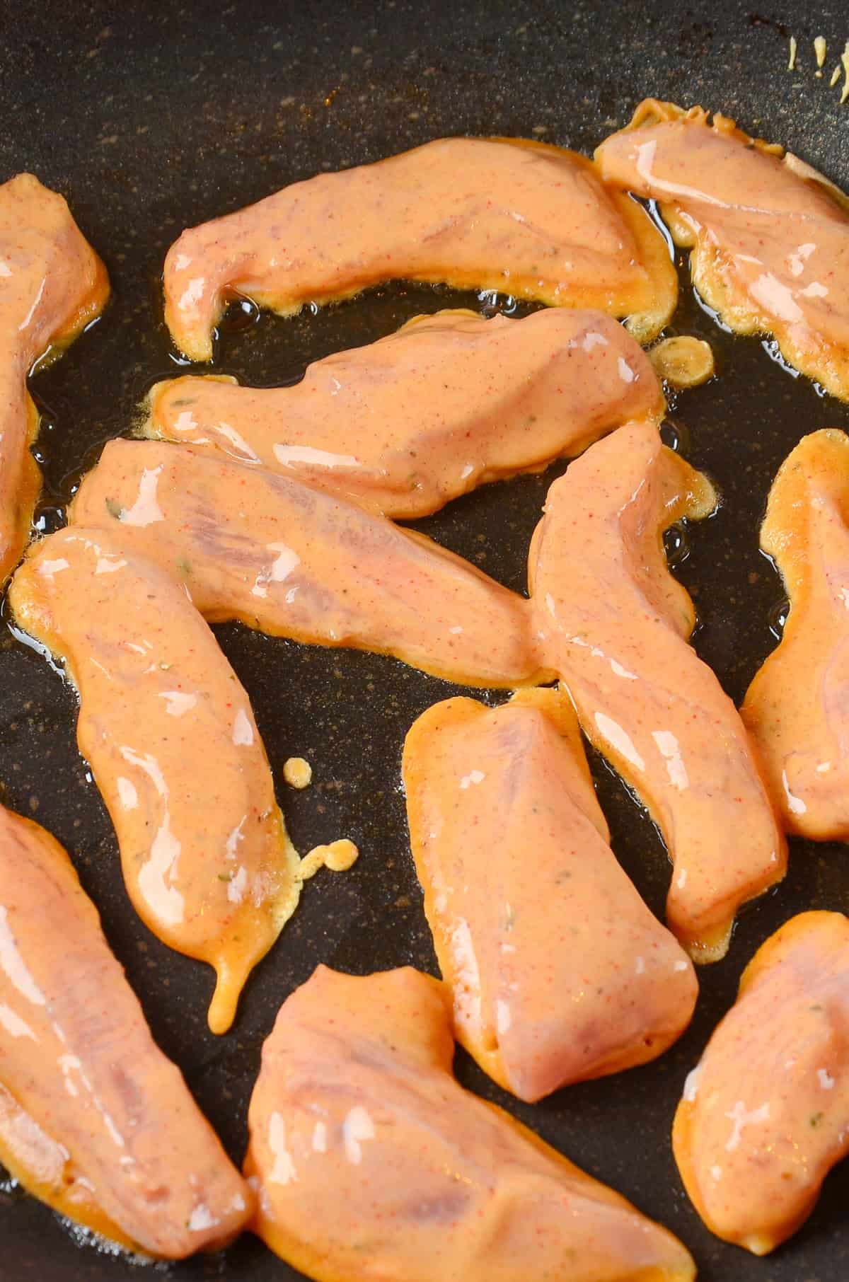 Battered chicken tenders cooking in a pan.