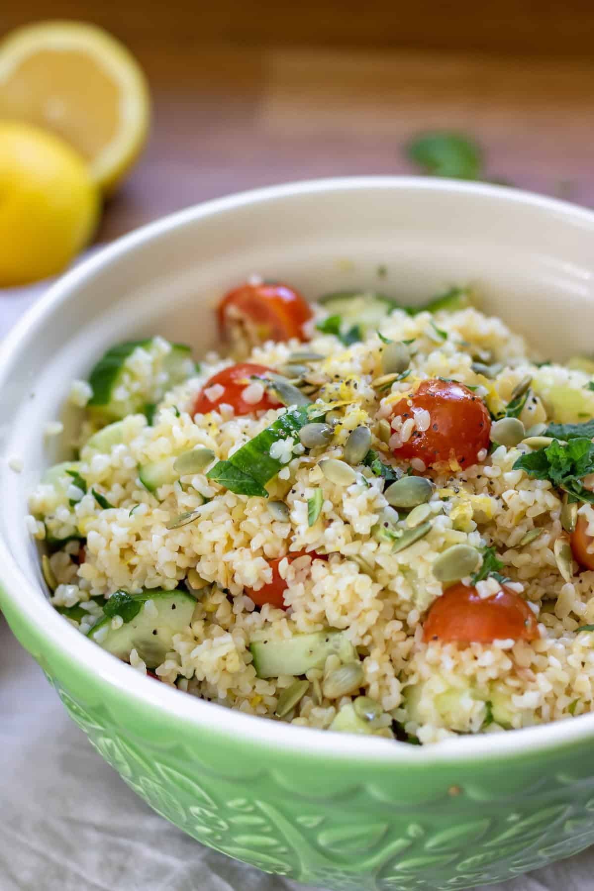 Bowl of bulgur salad with tomatoes, cucumber, pumpkin seeds, and lemon dressing.
