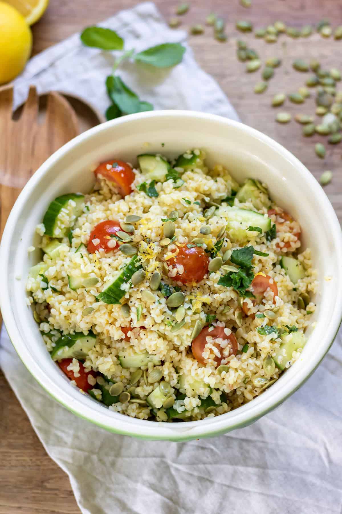 Bowl of bulgur salad with tomatoes, cucumber, pumpkin seeds, and lemon dressing.