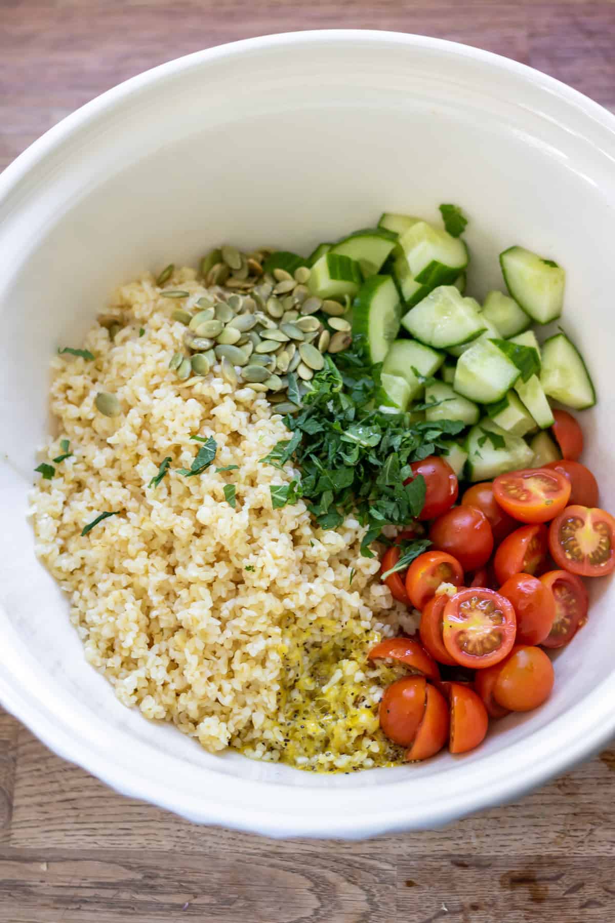 A bowl with the cooked bulgur, chopped vegetables, herbs, pumpkin seeds and lemon dressing.