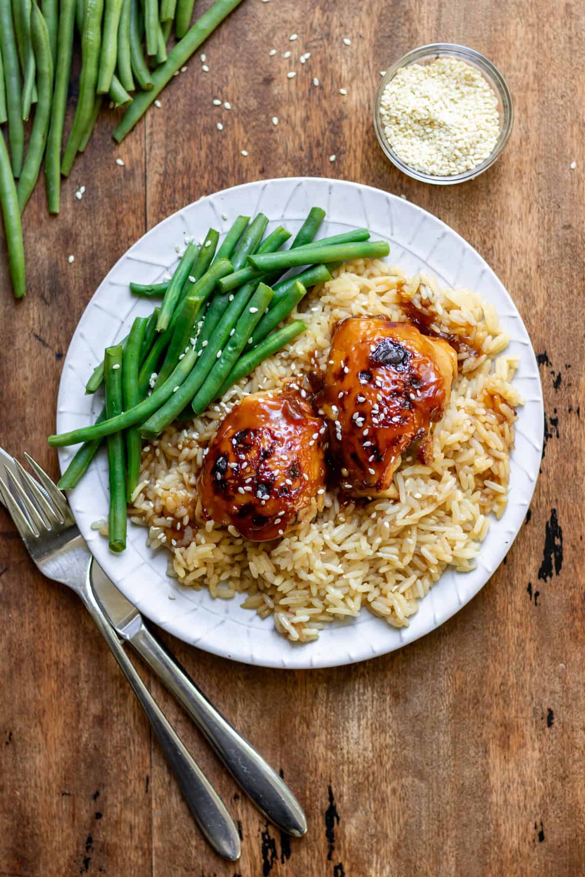 Looking down at a wooden table with a place of green beans and sticky honey soy chicken rice bake.