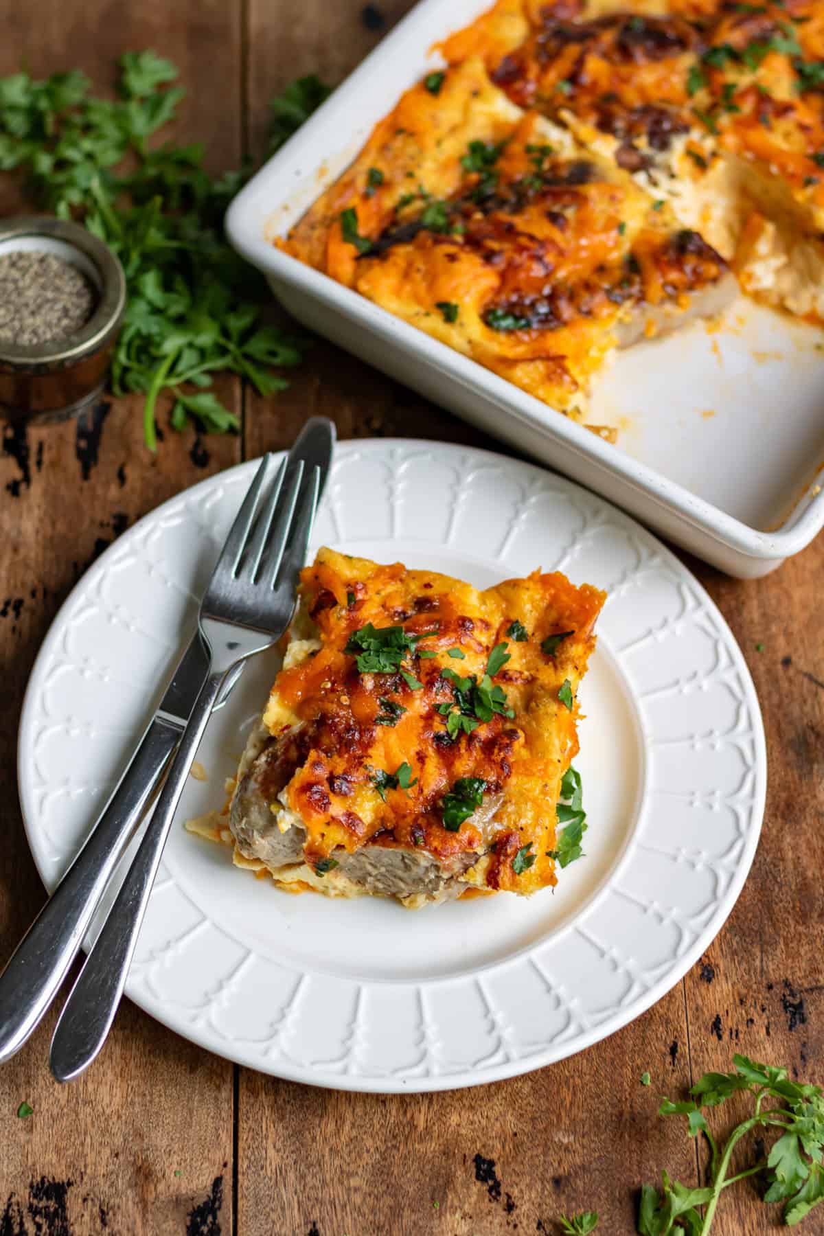 Looking down at a table with a serving dish of hot honey sausage breakfast bake with a slice of it on a plate next to it.