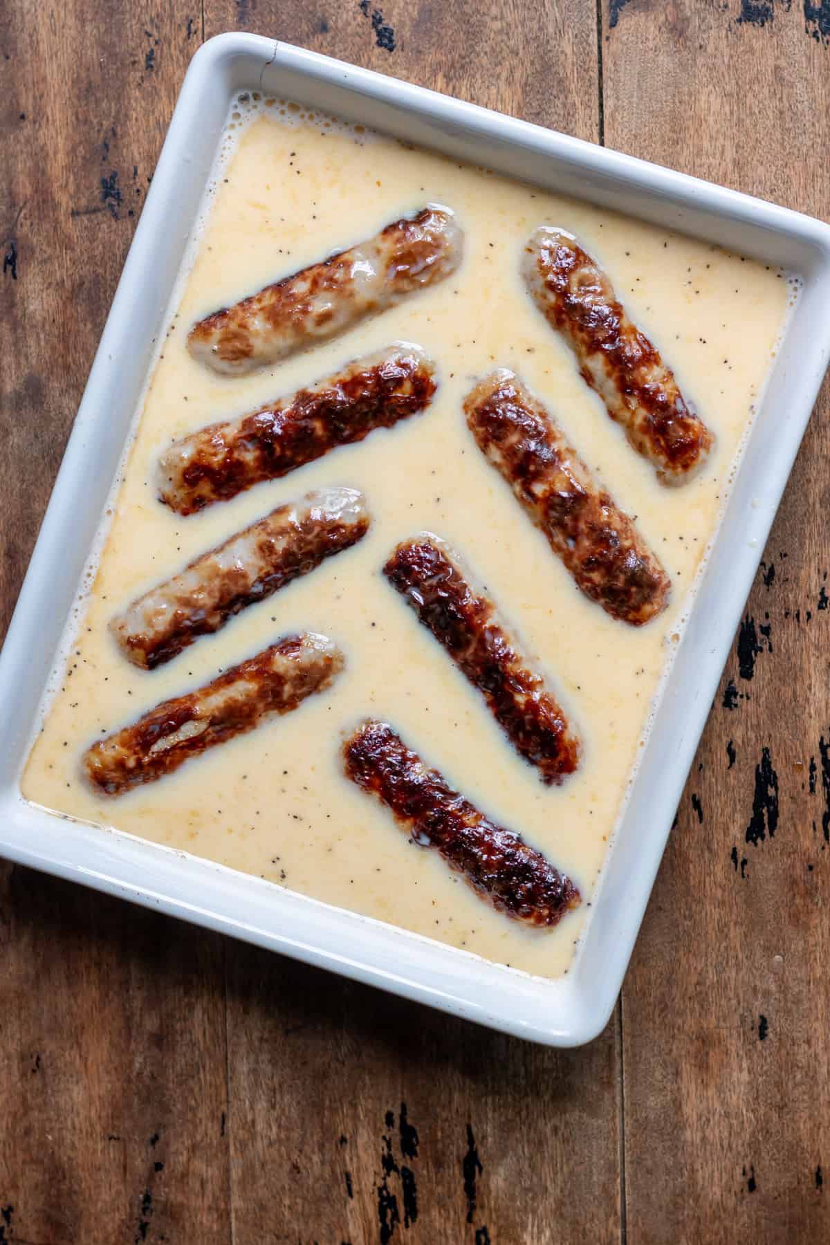 Browned sausages placed into the baking dish of beaten eggs.