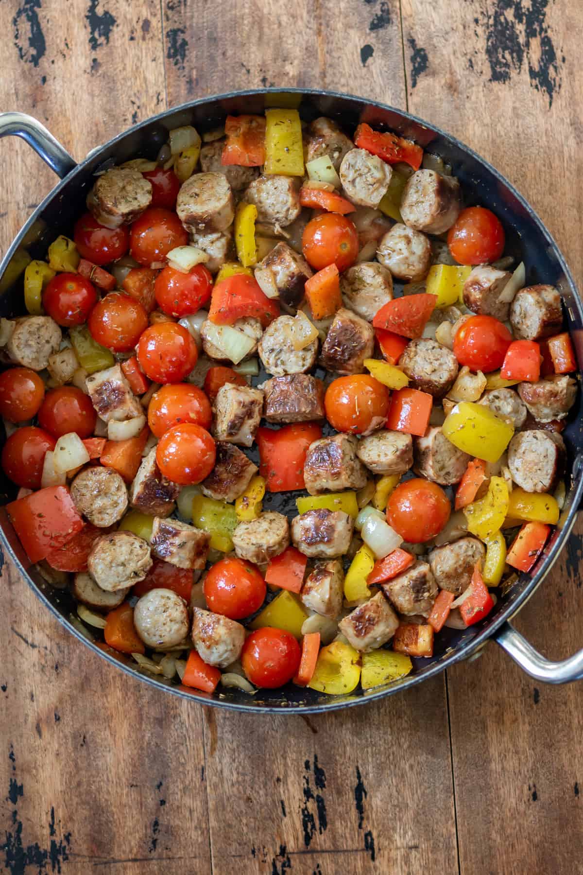 Cooked sausages, peppers and onions in a skillet.
