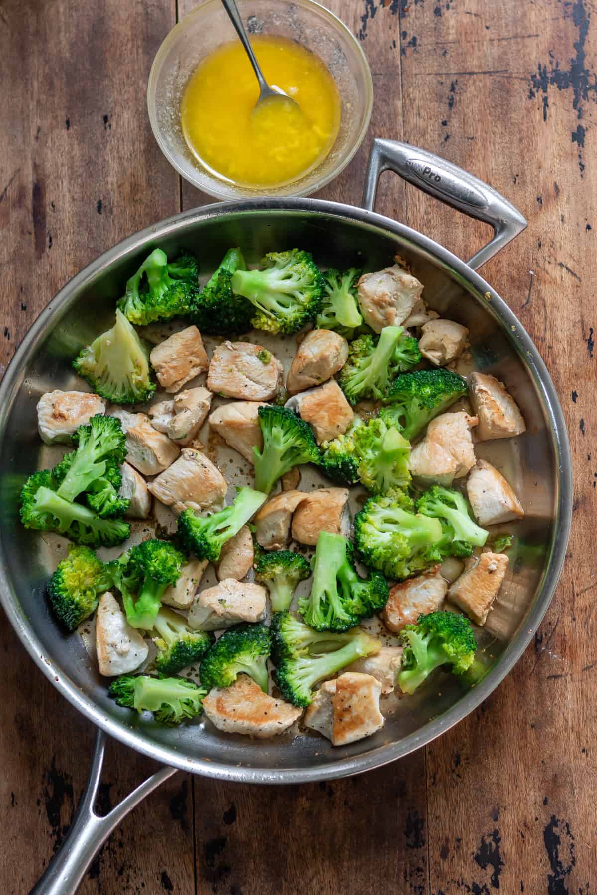 Drizzling the garlic butter over the cooked chicken and broccoli skillet.