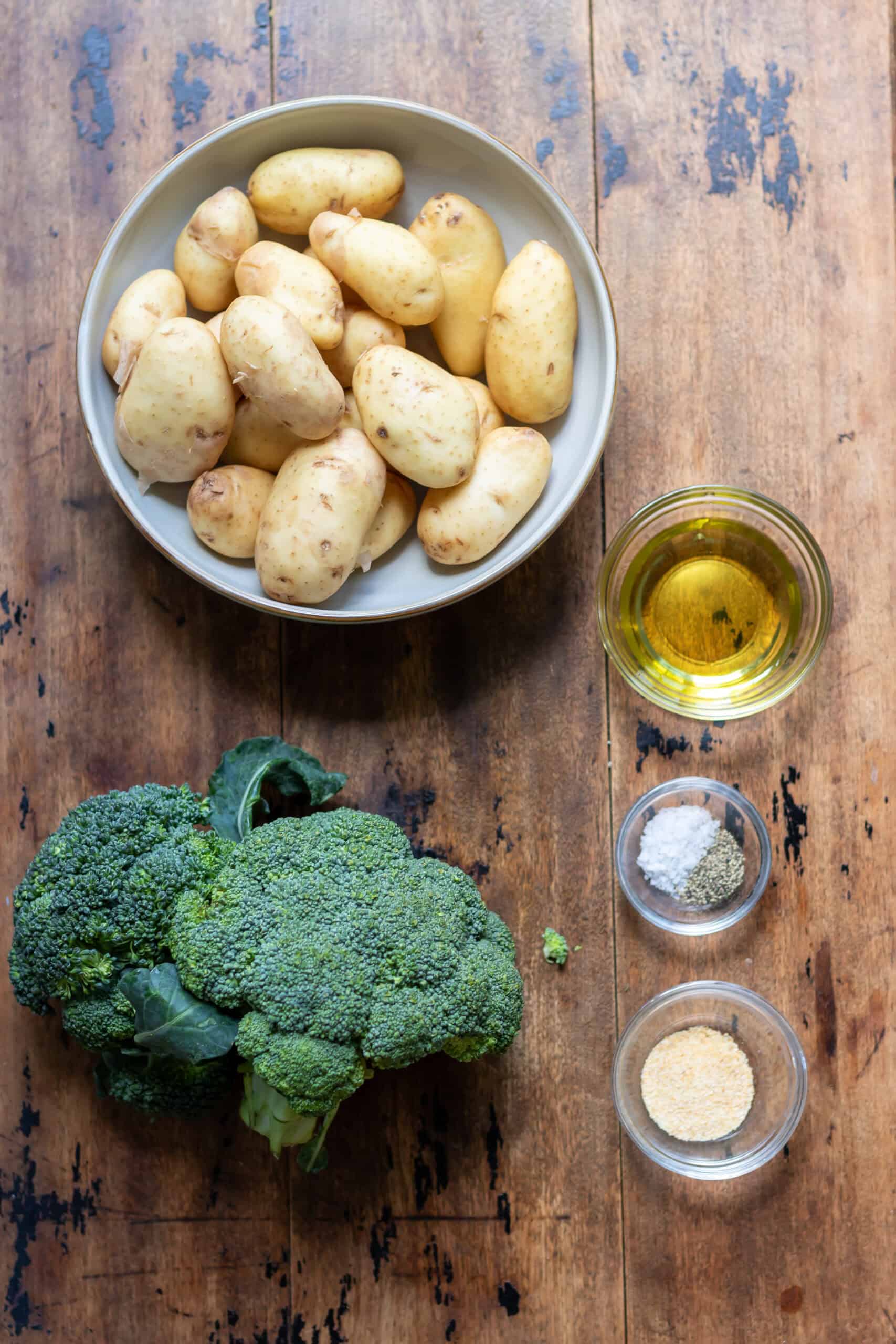 Broccoli, baby potatoes, oil, garlic powder, salt and pepper on a table.