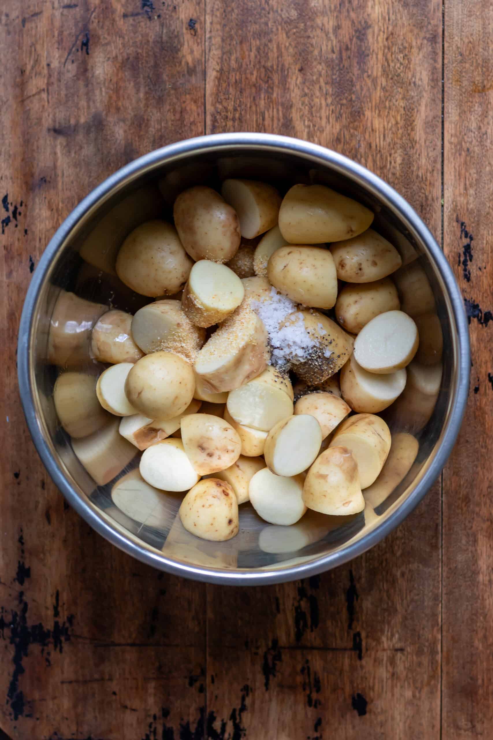 A bowl with halved baby potatoes with oil and seasonings.