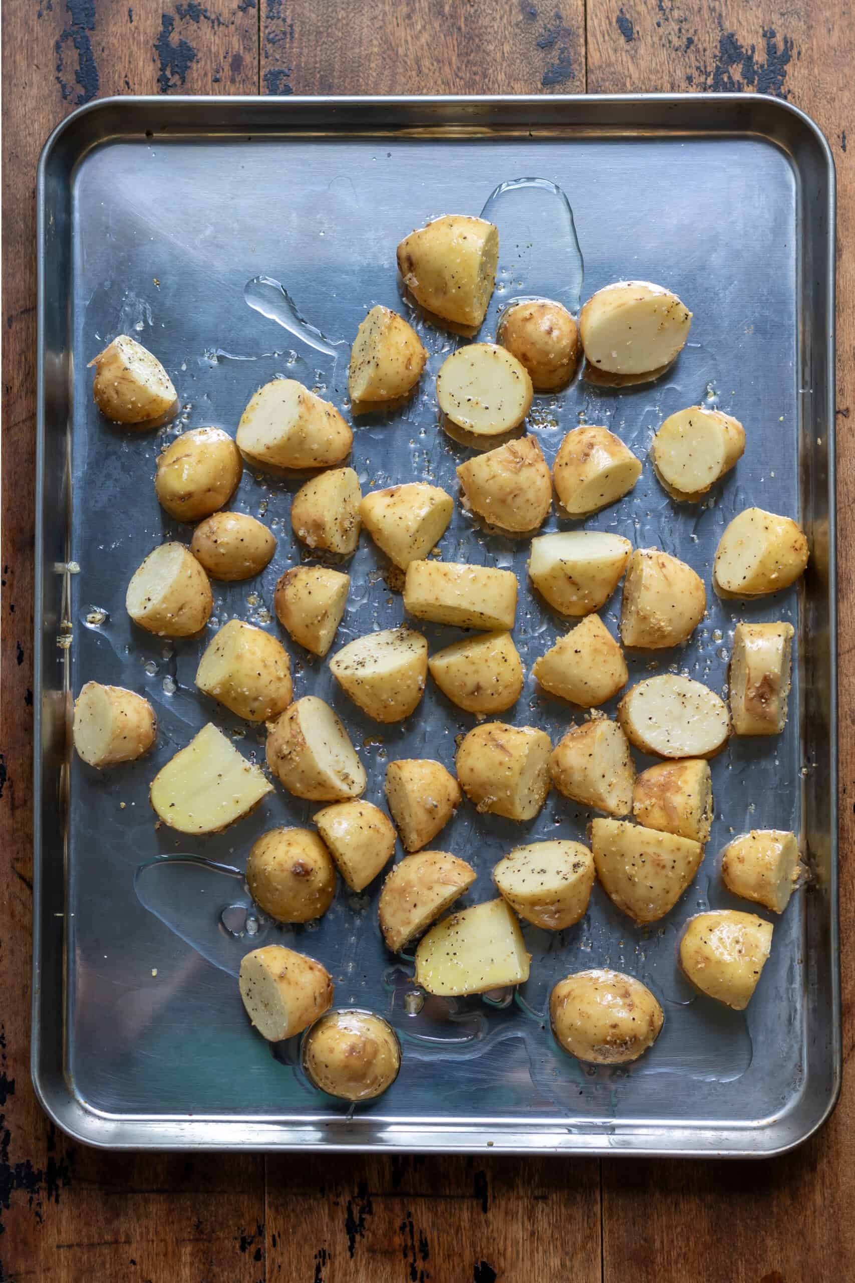 Seasoned potatoes on a baking sheet with oil.