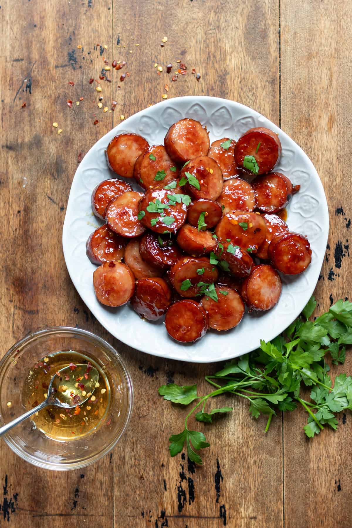 A wooden table with a plate of hot honey sausage bites, next to a bowl of hot honey.