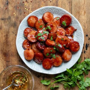 A wooden table with a plate of hot honey sausage bites, next to a bowl of hot honey.