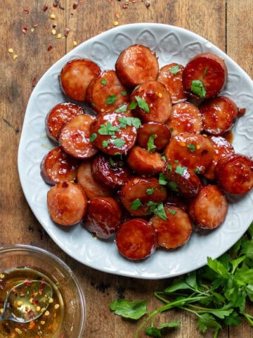 A wooden table with a plate of hot honey sausage bites, next to a bowl of hot honey.