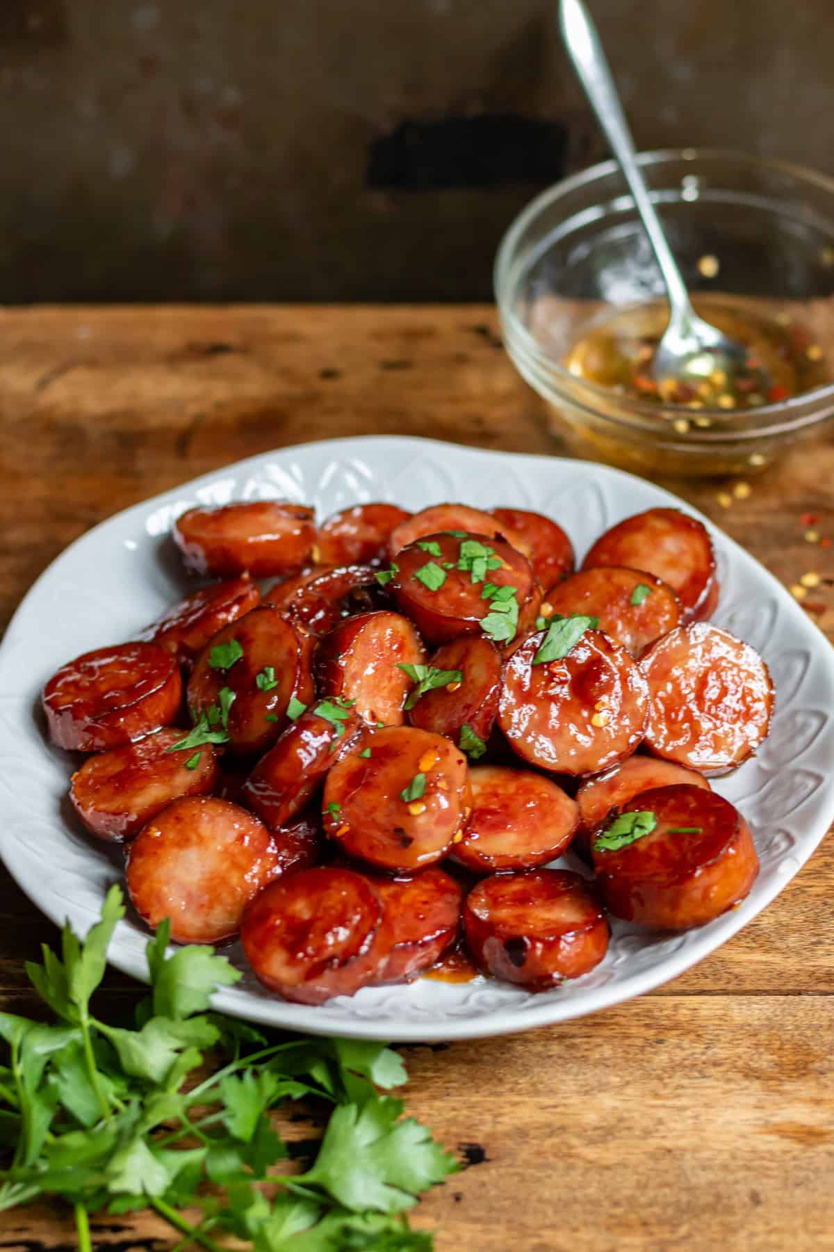 A table with a serving plate of sliced smoked sausage bites in hot honey.