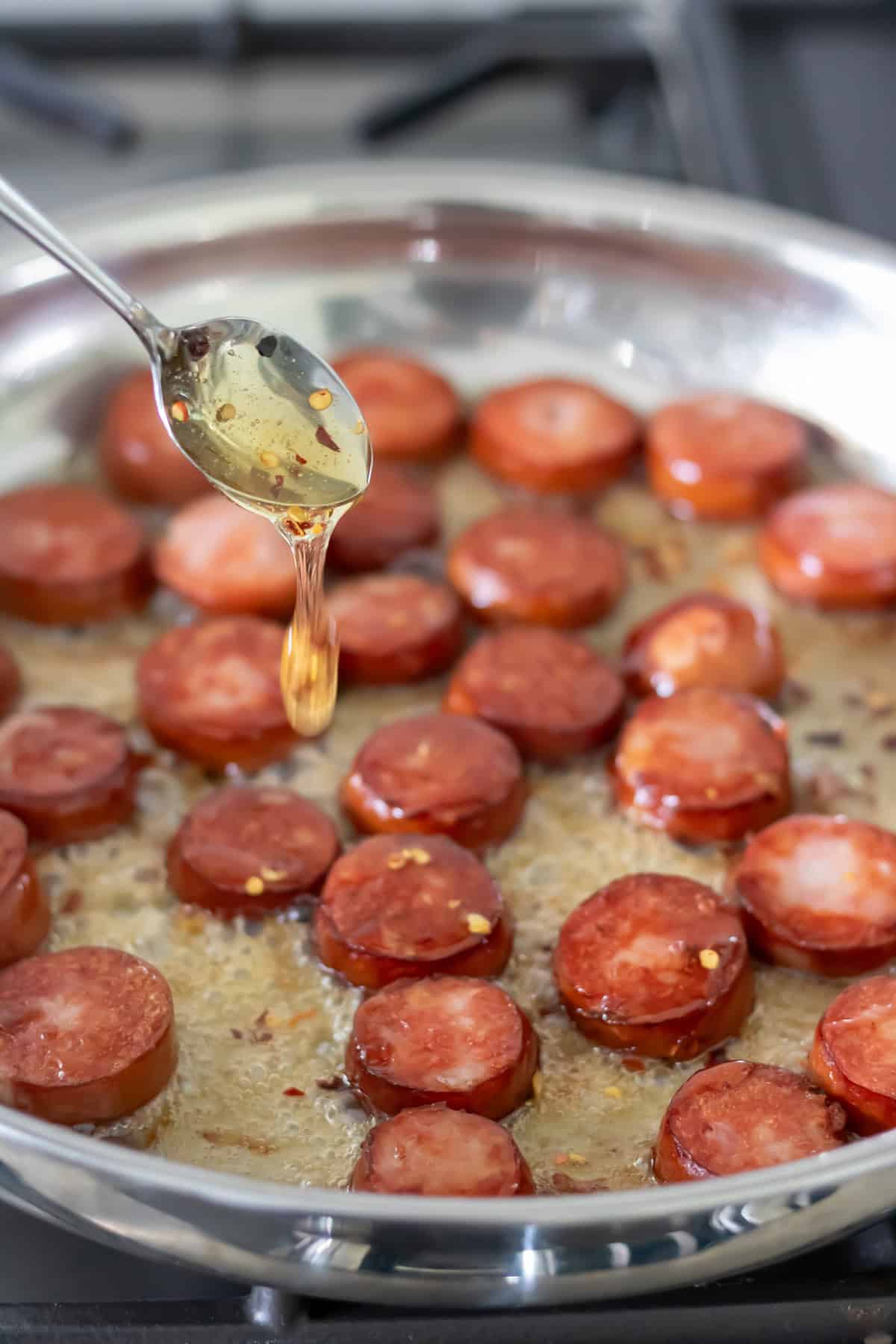 Adding the hot honey to the cooked sliced smoked sausages in a pan.
