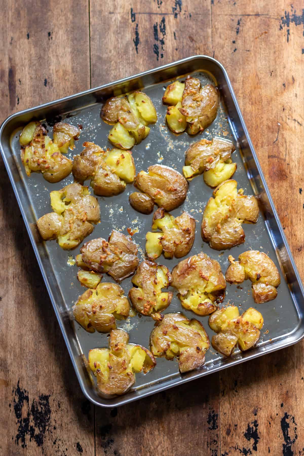 A wooden table with a baking sheet of smashed roasted baby potatoes.