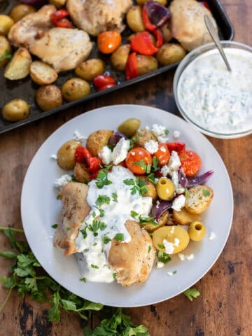 A table with a sheet pan of roasted chicken, potatoes and vegetables, with a portion on a plate.