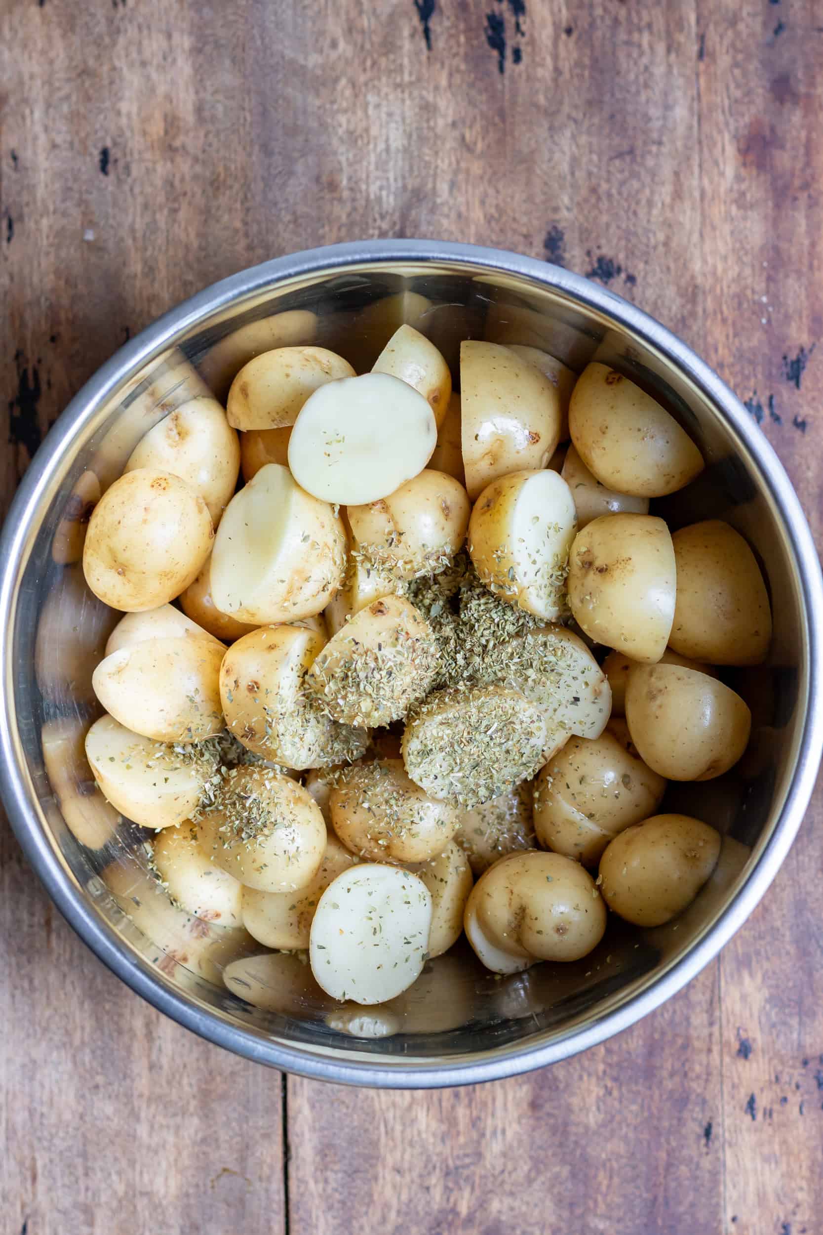 Halved baby potatoes in a bowl with seasonings.