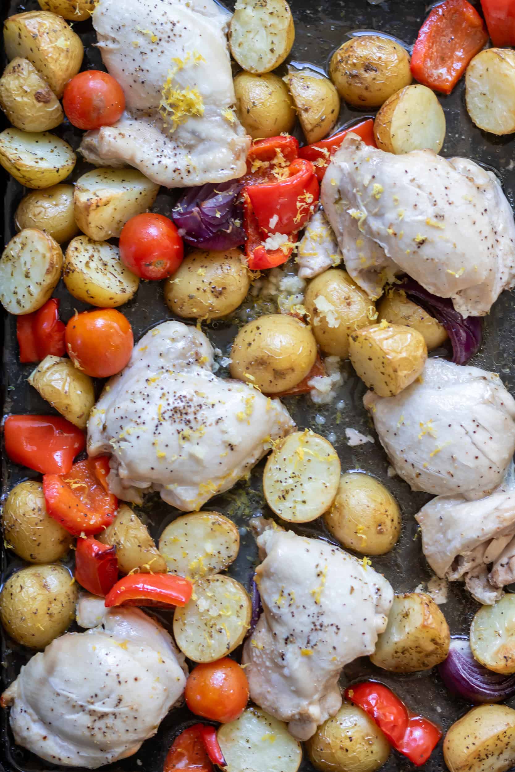 Chicken thighs, onions, peppers, tomatoes, garlic and lemon with the potatoes on the sheet pan.