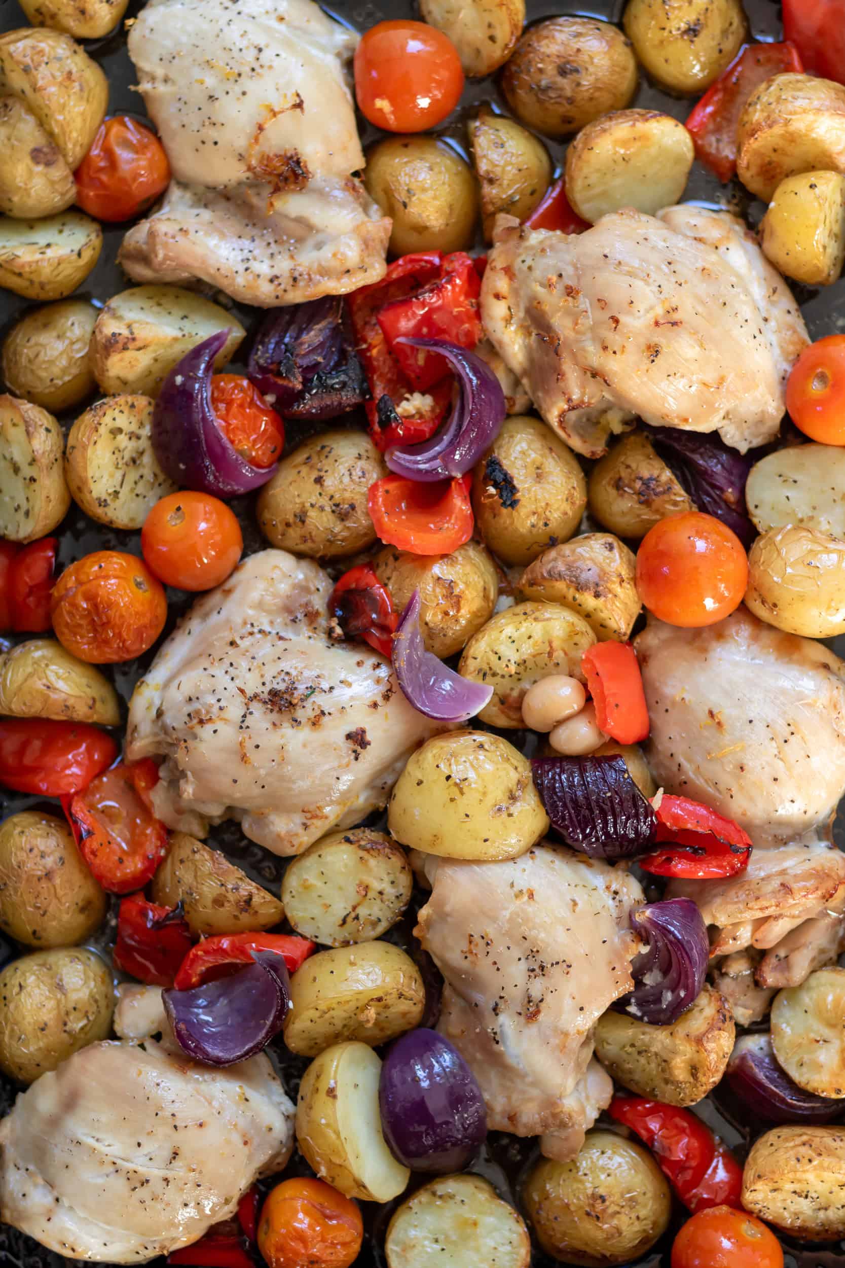 Roasted Greek chicken and potatoes on a sheet pan with vegetables.