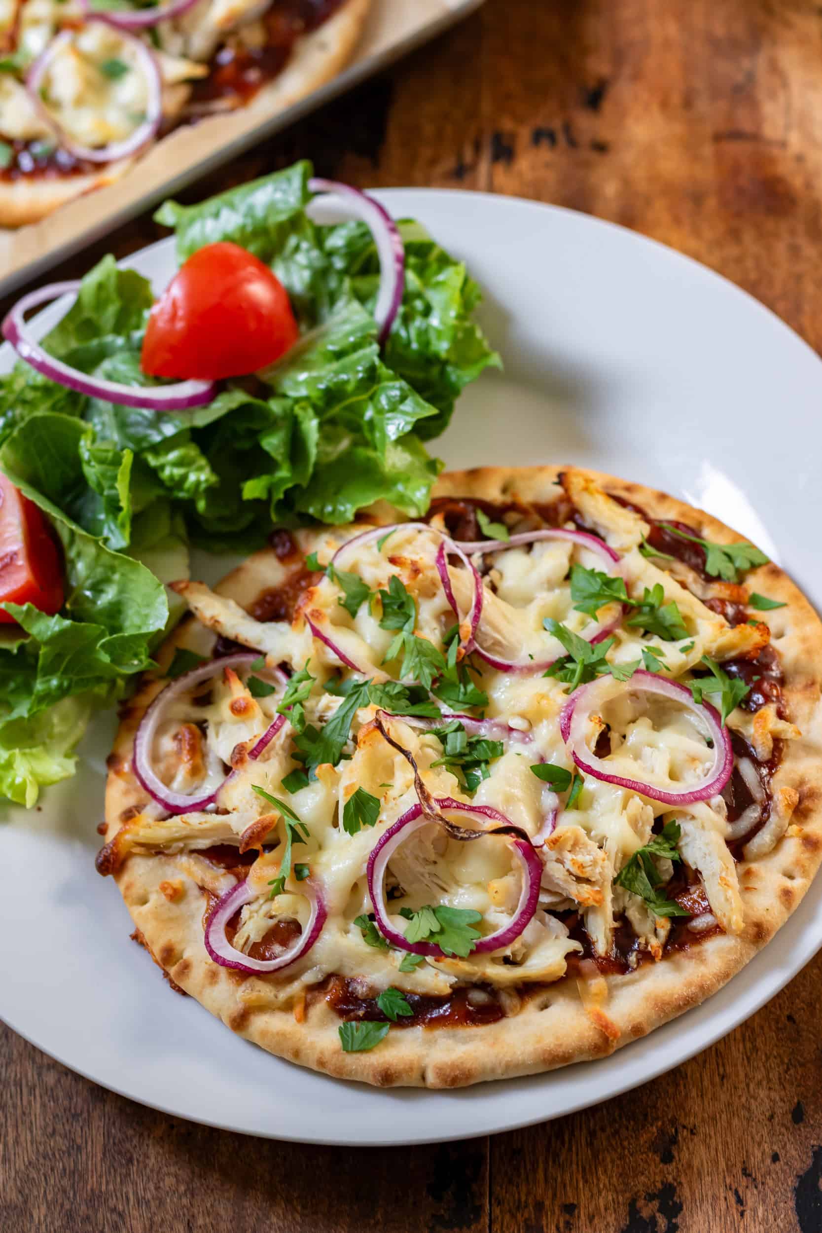 A plate with a barbecue chicken flatbread and salad.