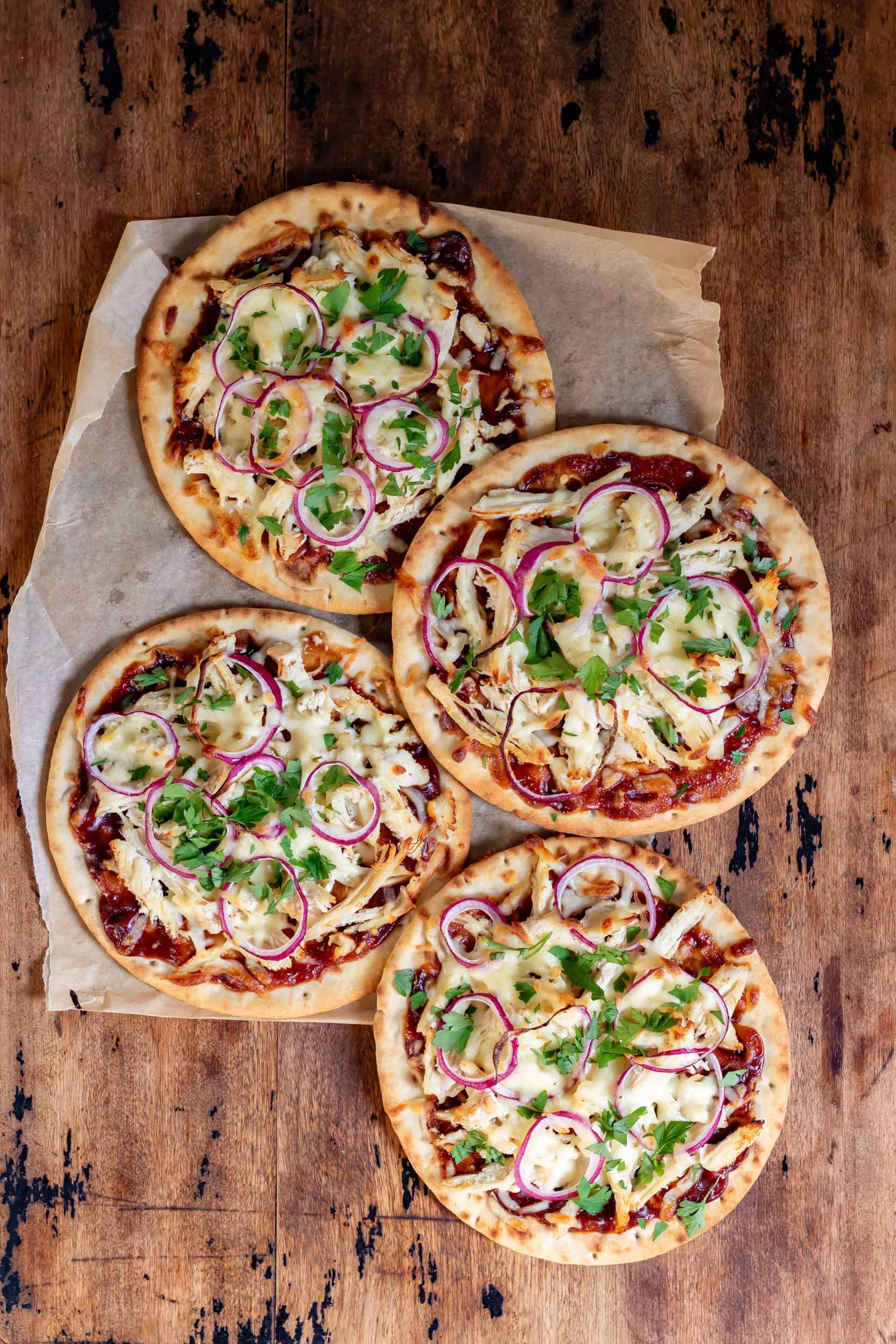 A wooden table with four bbq chicken flatbreads.