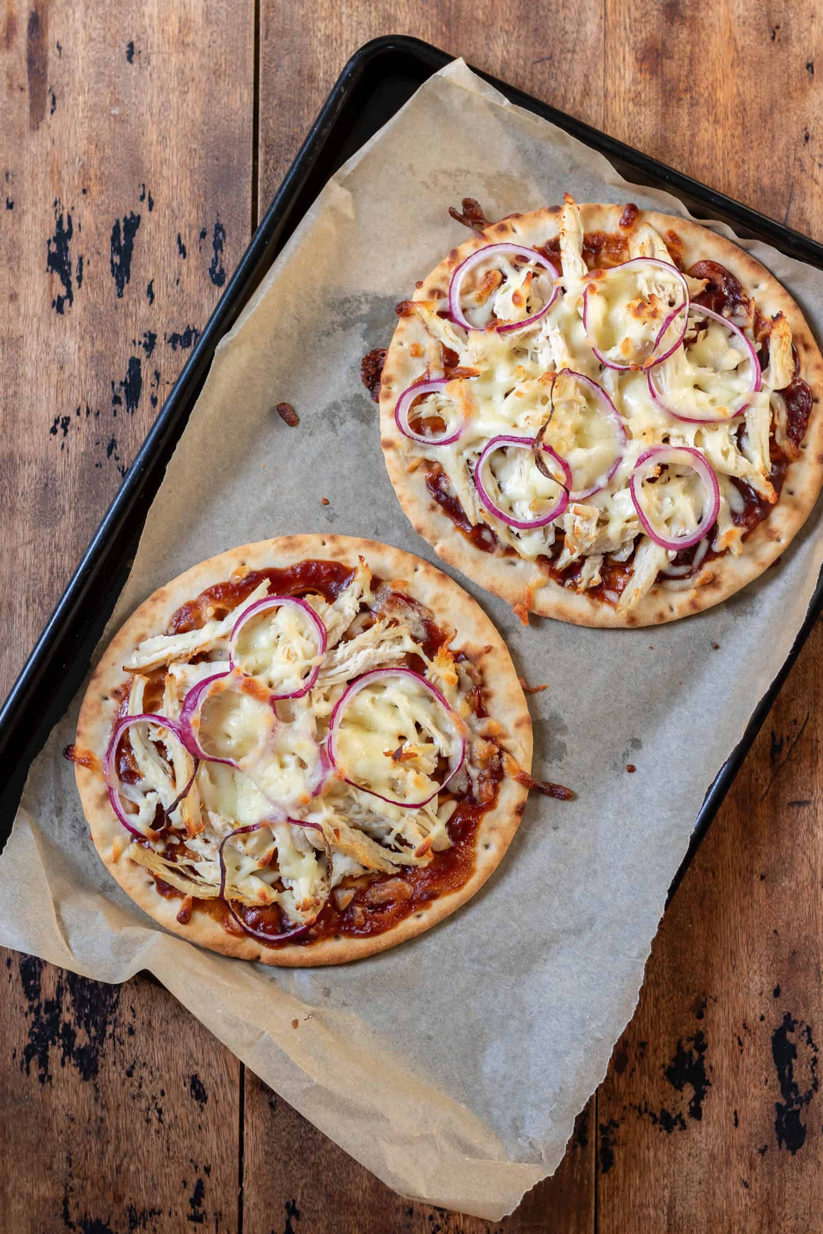 A baking sheet on a table with two cooked bbq chicken flatbreads.
