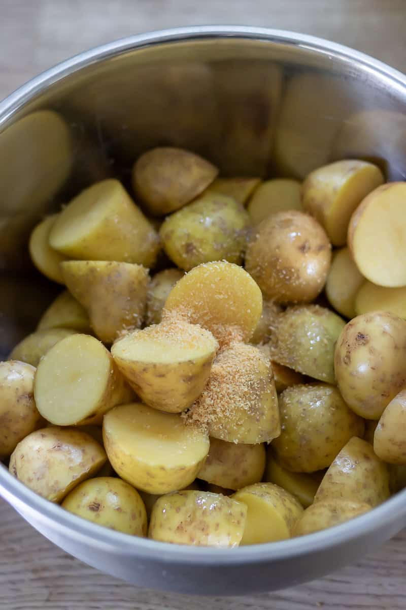Seasonings added to a bowl of cut baby potatoes.