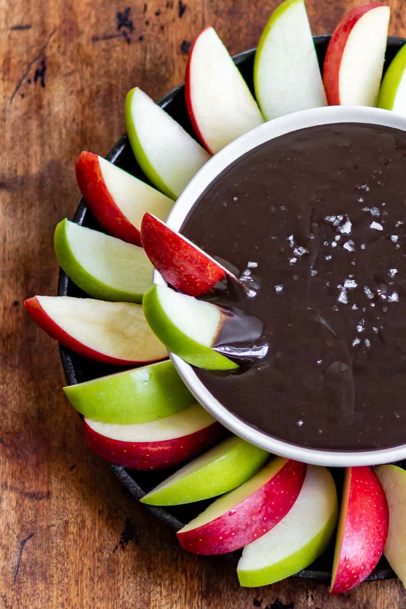 Close up of two apple slices dipped into a bowl of Halloween black cocoa caramel dip.