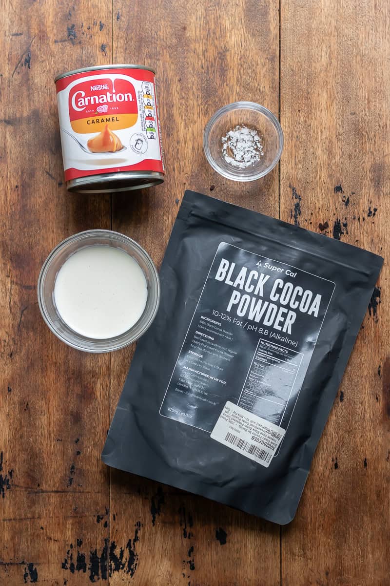 Black cocoa powder, heavy cream, caramel in a can, and sea salt on a table.